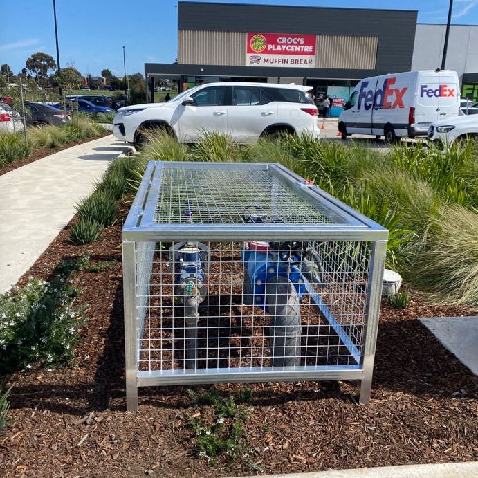 Custom galvanised steel protection cage installed over an RPZ valve in a retail car park